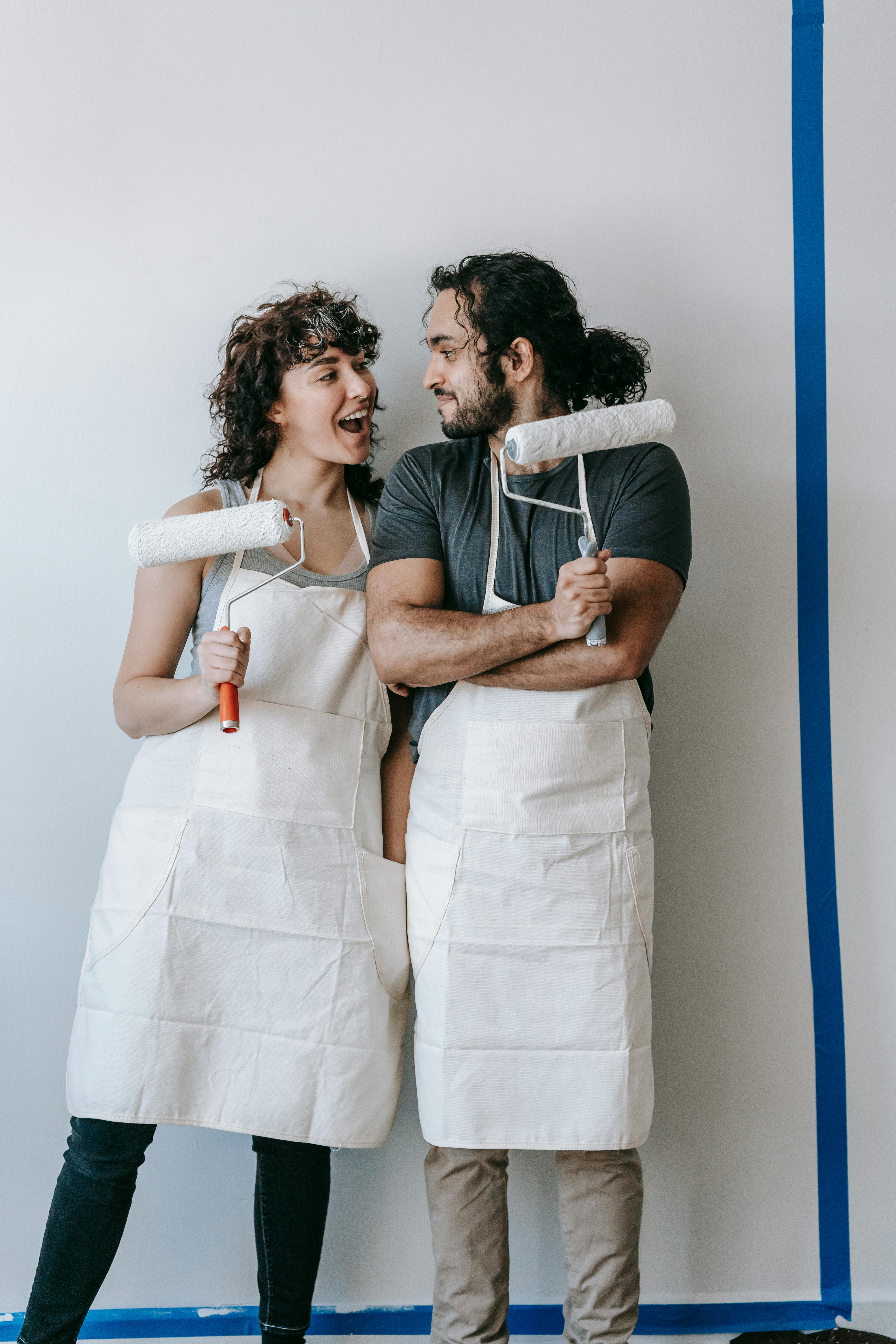 Energetic young couple laughing while painting their apartment walls together.