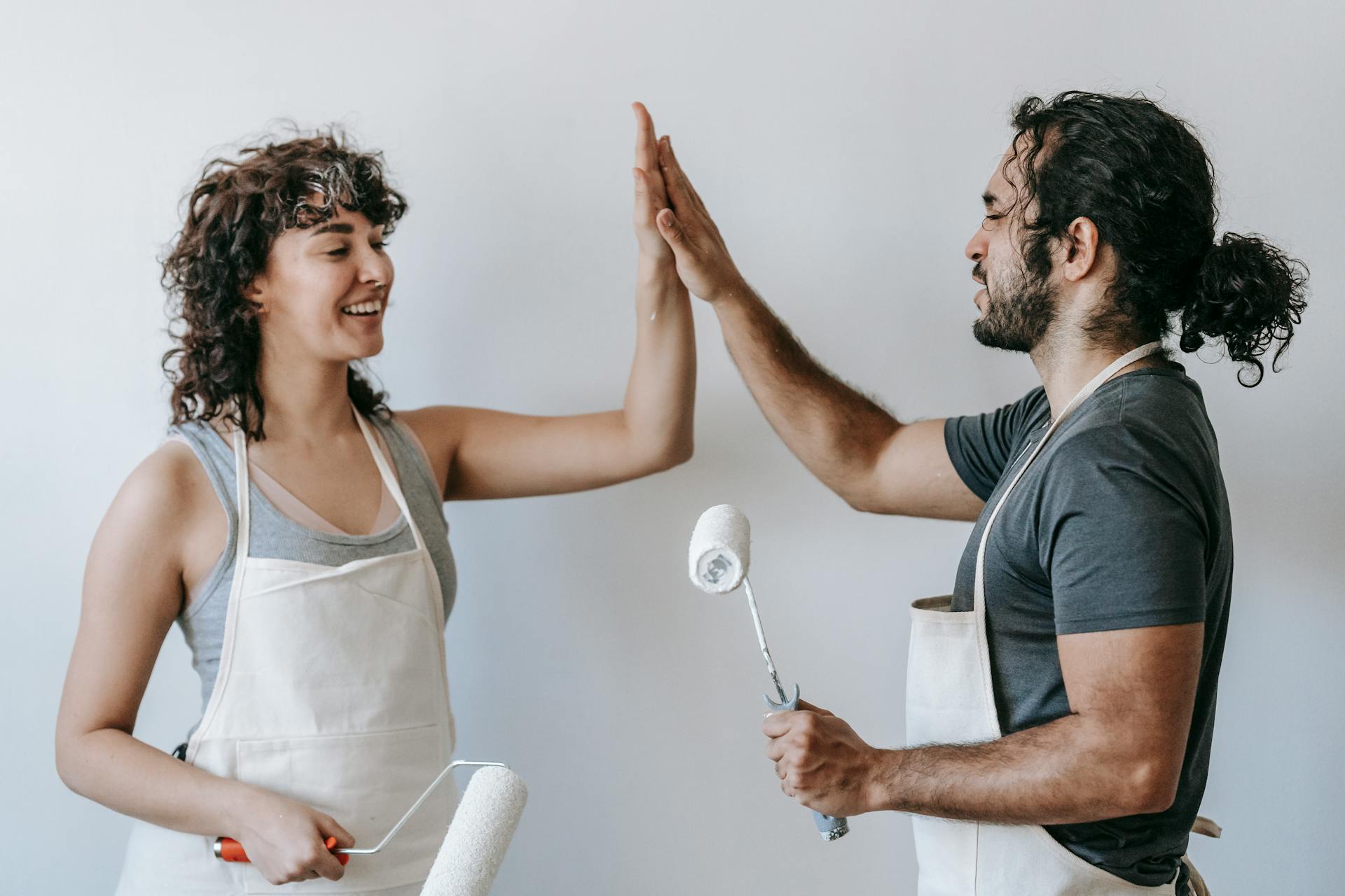 Happy couple high-fiving during home painting project, celebrating teamwork and renovation success.