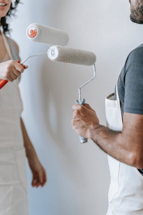 rop Photo Of Couple Standing Face To Face Holding Paint Rollers