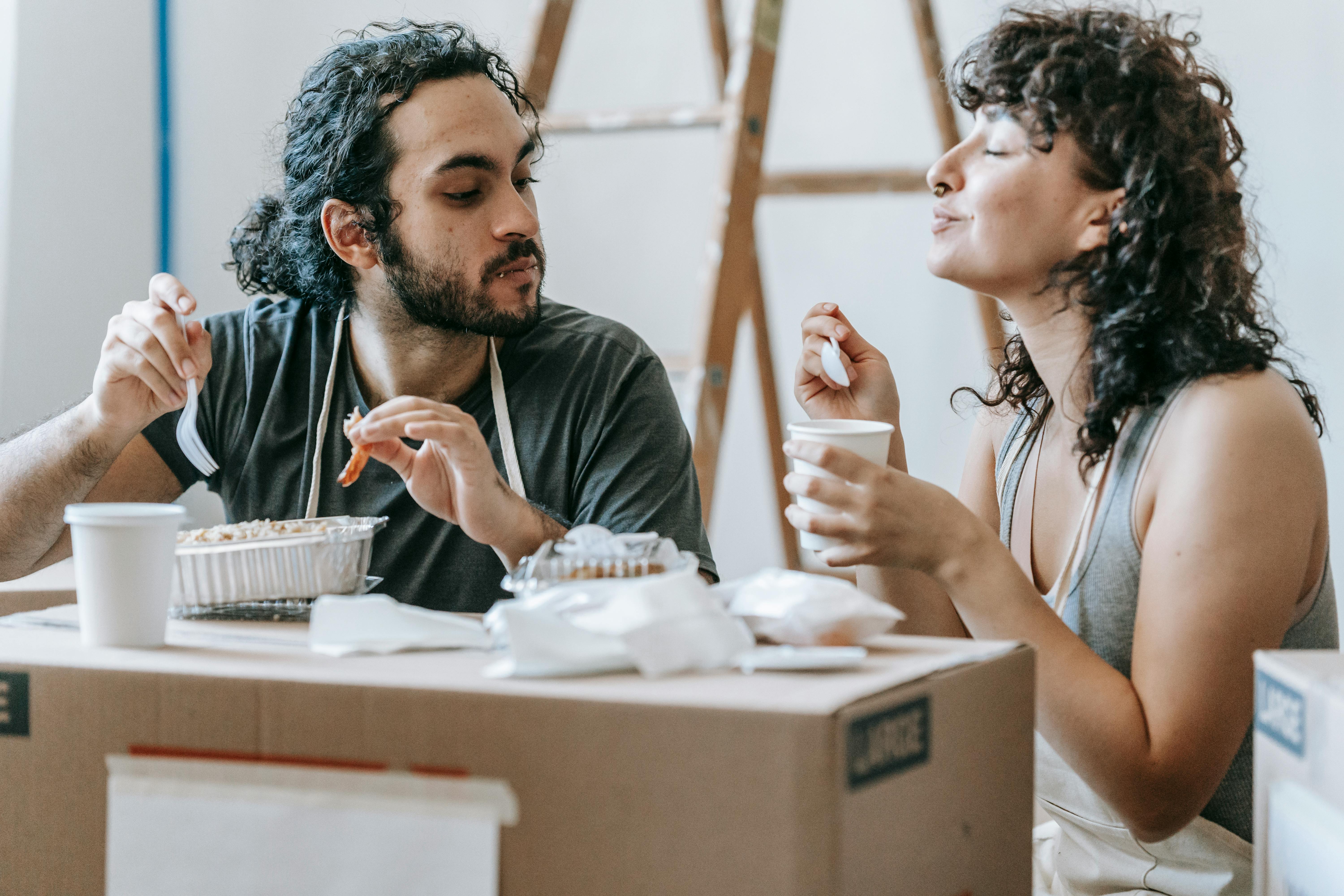 ethnic couple enjoying delicious takeaway lunch in renovated house
