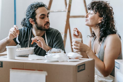 Ethnic couple enjoying delicious takeaway lunch in renovated house