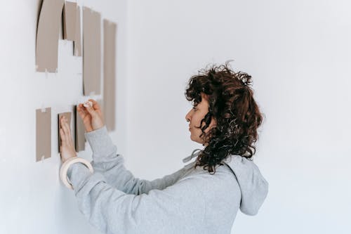 Woman in Gray Long Sleeve Shirt Putting A Cardboard On Wall