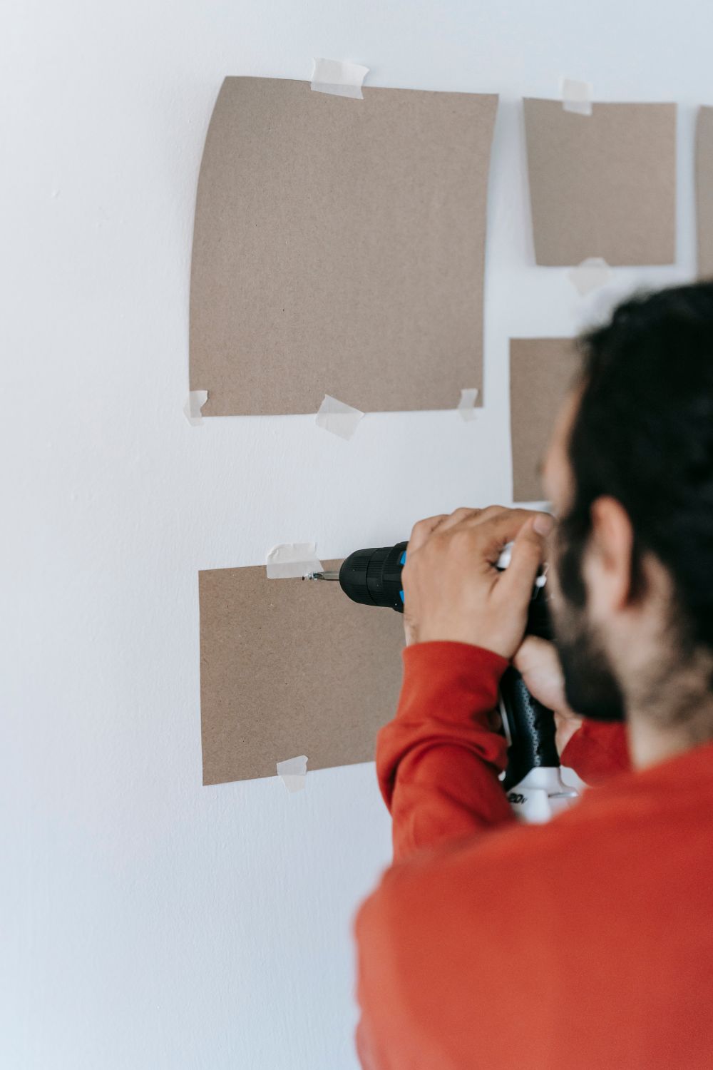 A person fixing a screw into a wall with an electric screwdriver at home