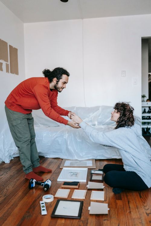 Free A couple organizing picture frames on the wooden floor of a living room, planning their home decor. Stock Photo