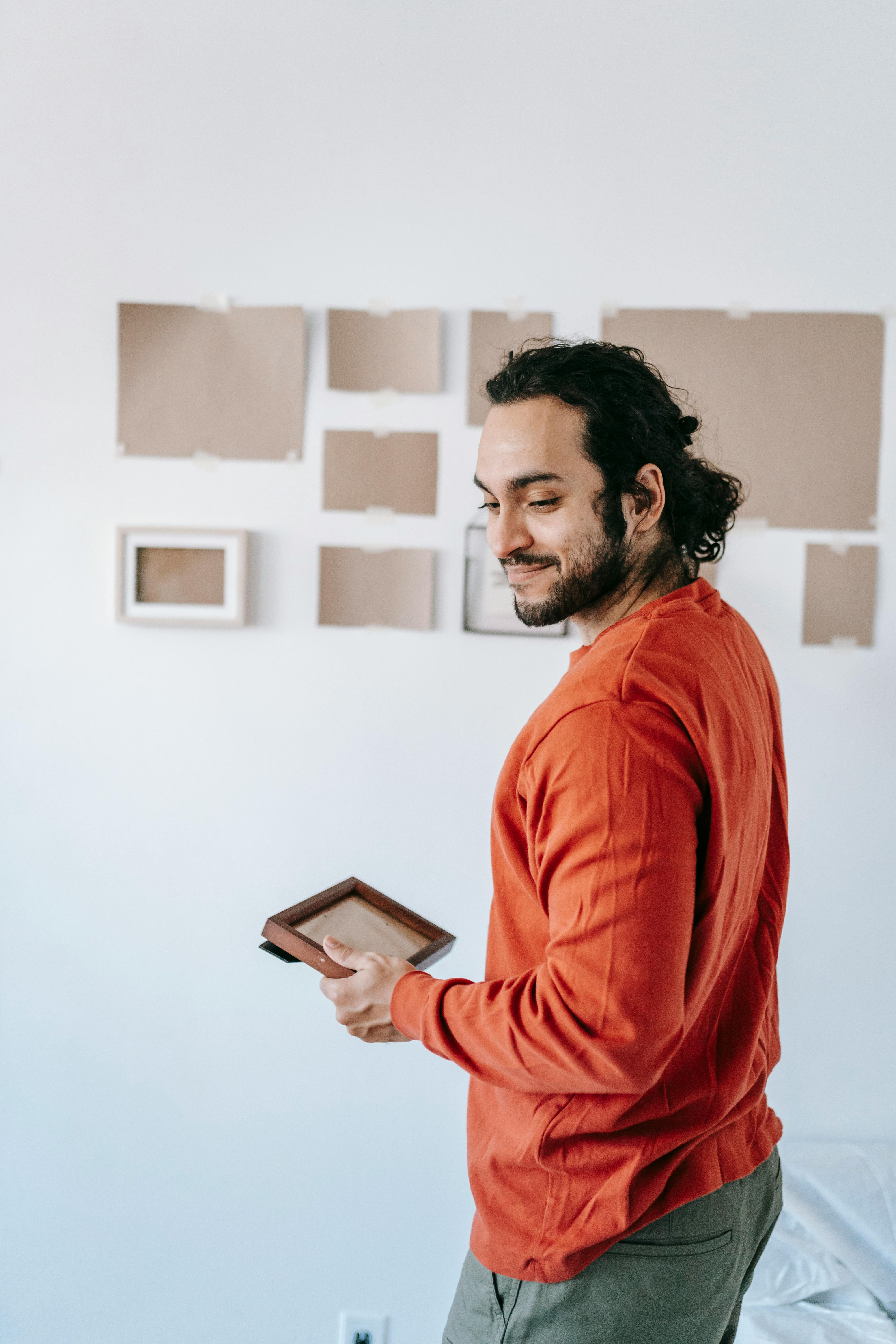 A smiling young man adjusts picture frames on a wall during home improvement.