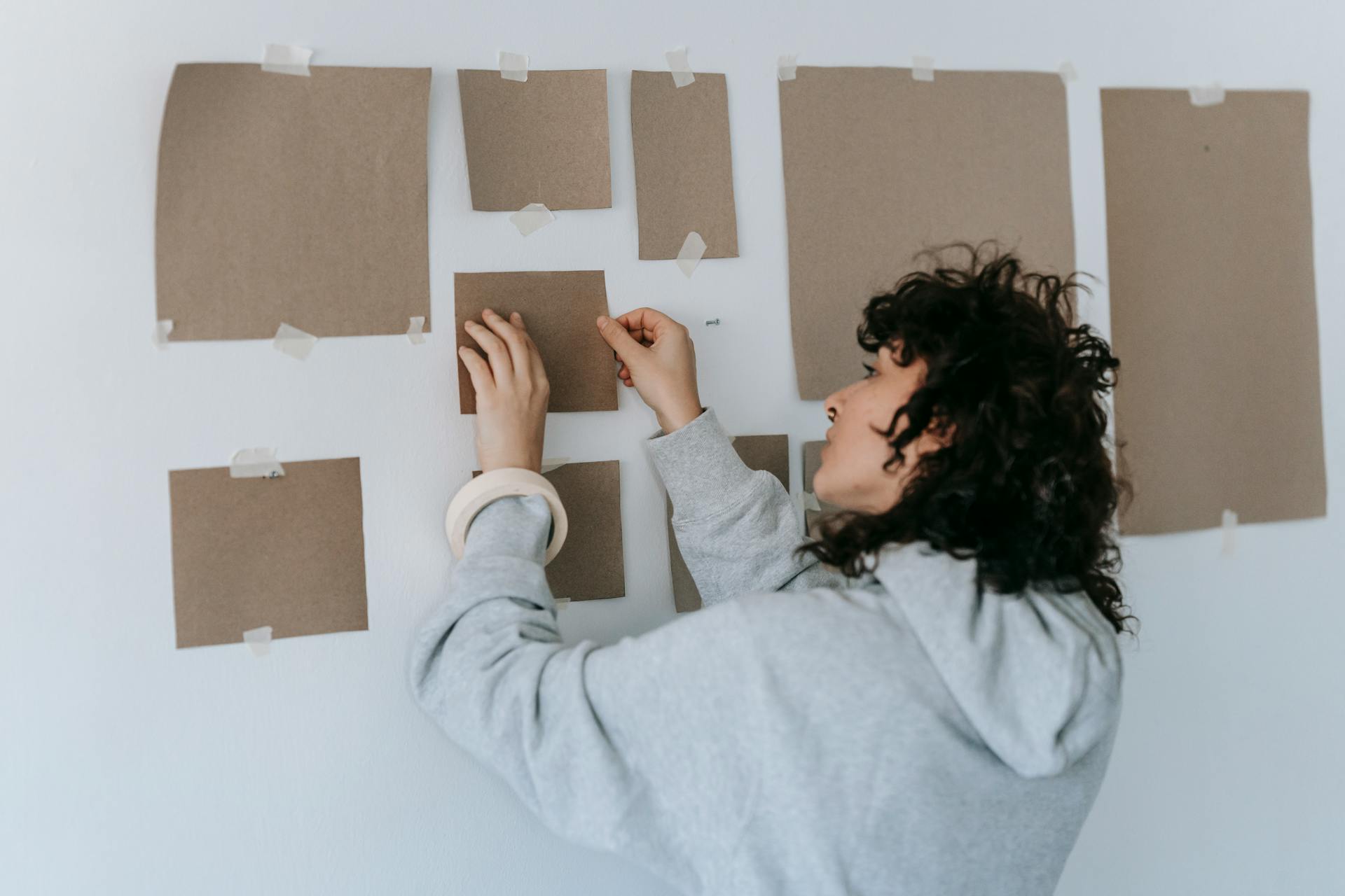 Woman in Gray Long Sleeve Shirt Removing Paper From Wall