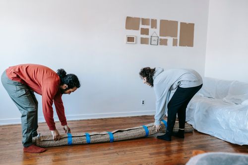Free Two adults carefully roll up a rug while packing up in a bright, minimal living room. Stock Photo