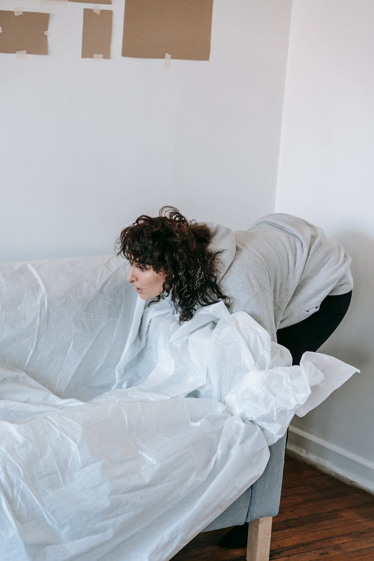 Woman Covering A Couch With White Plastic