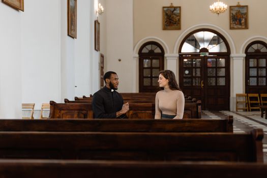 Priest and Woman Sitting on Church Pew Having a Conversation