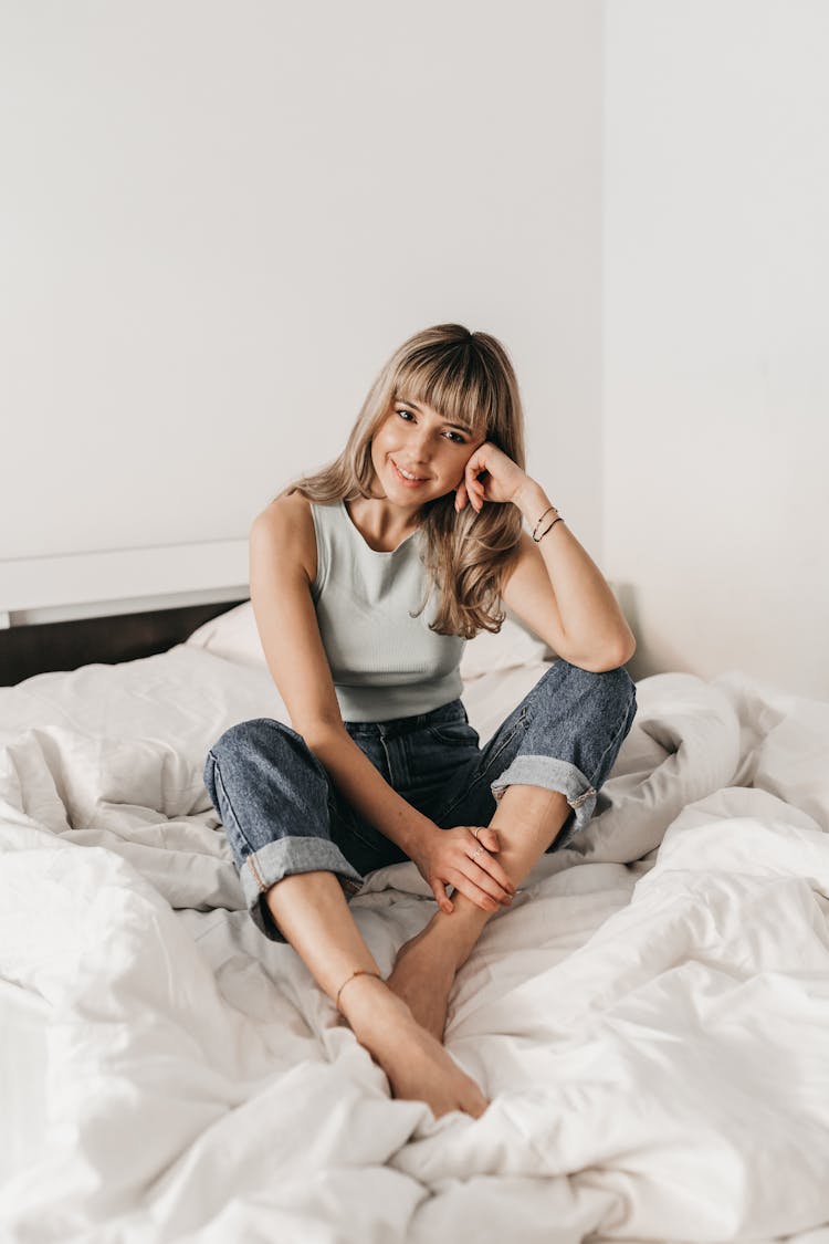 Smiling Woman Leaning On Hand On Unmade Bed At Home