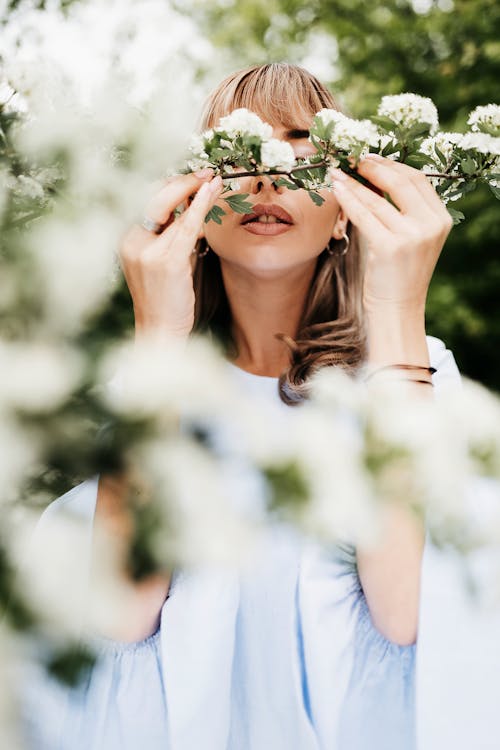 Tender female enjoying aroma of blossoming flowers on bush branch in spring on blurred background
