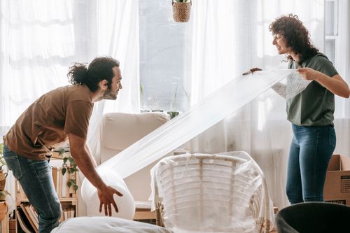 Free A couple joyfully packs furniture with bubble wrap in their bright living room. Stock Photo