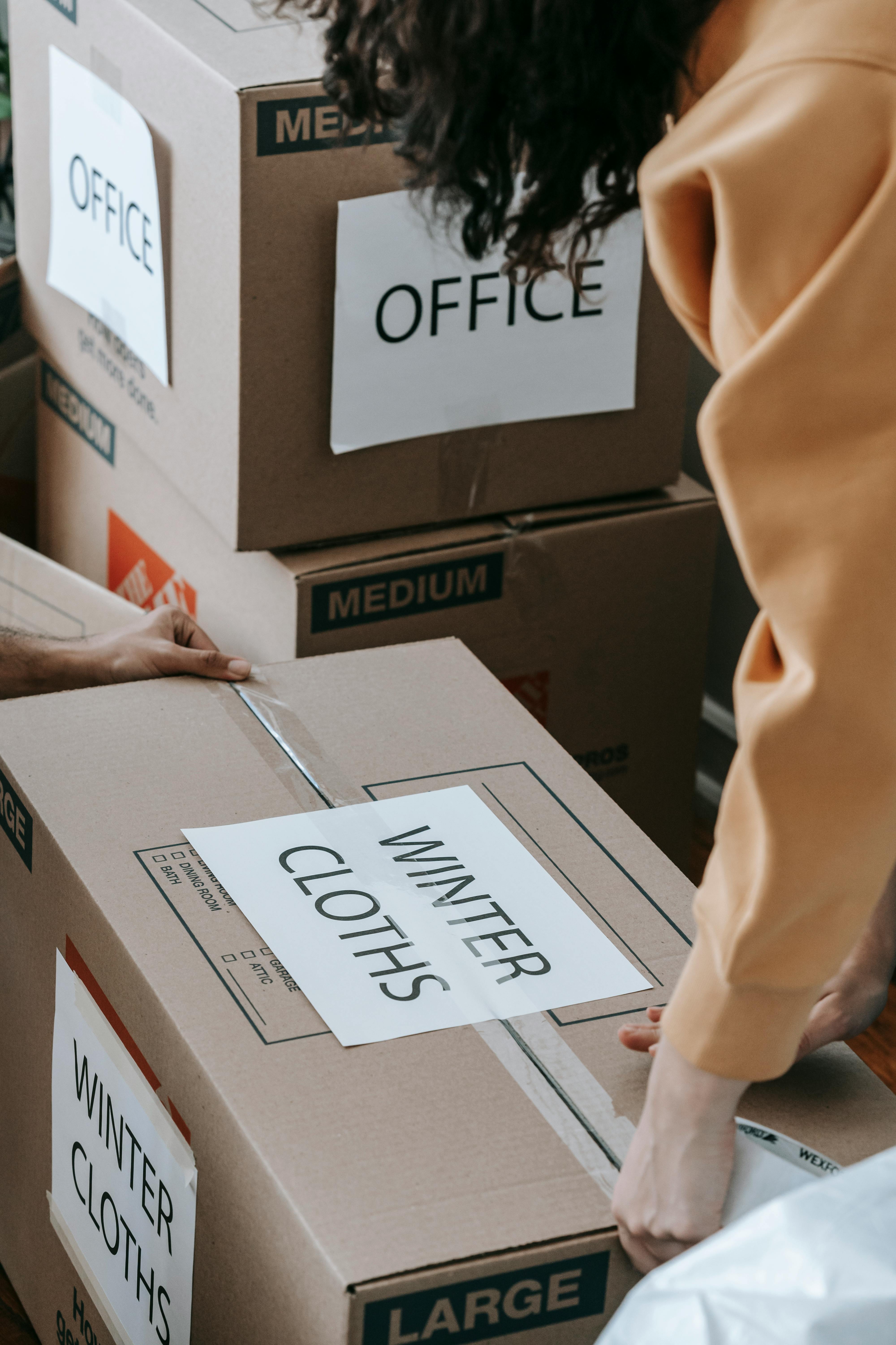 person in orange shirt sealing a box of winter clothes