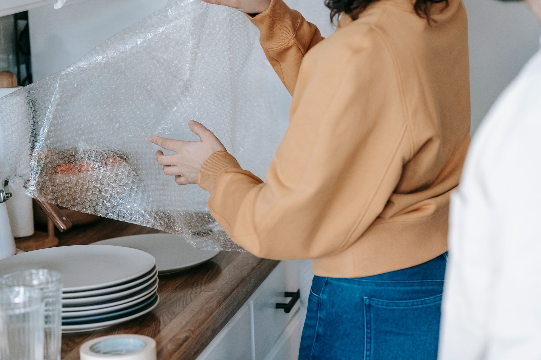 close-up photograph of ecommerce seller packing fragile product with bubble wrap and cardboard box on a clean workbench