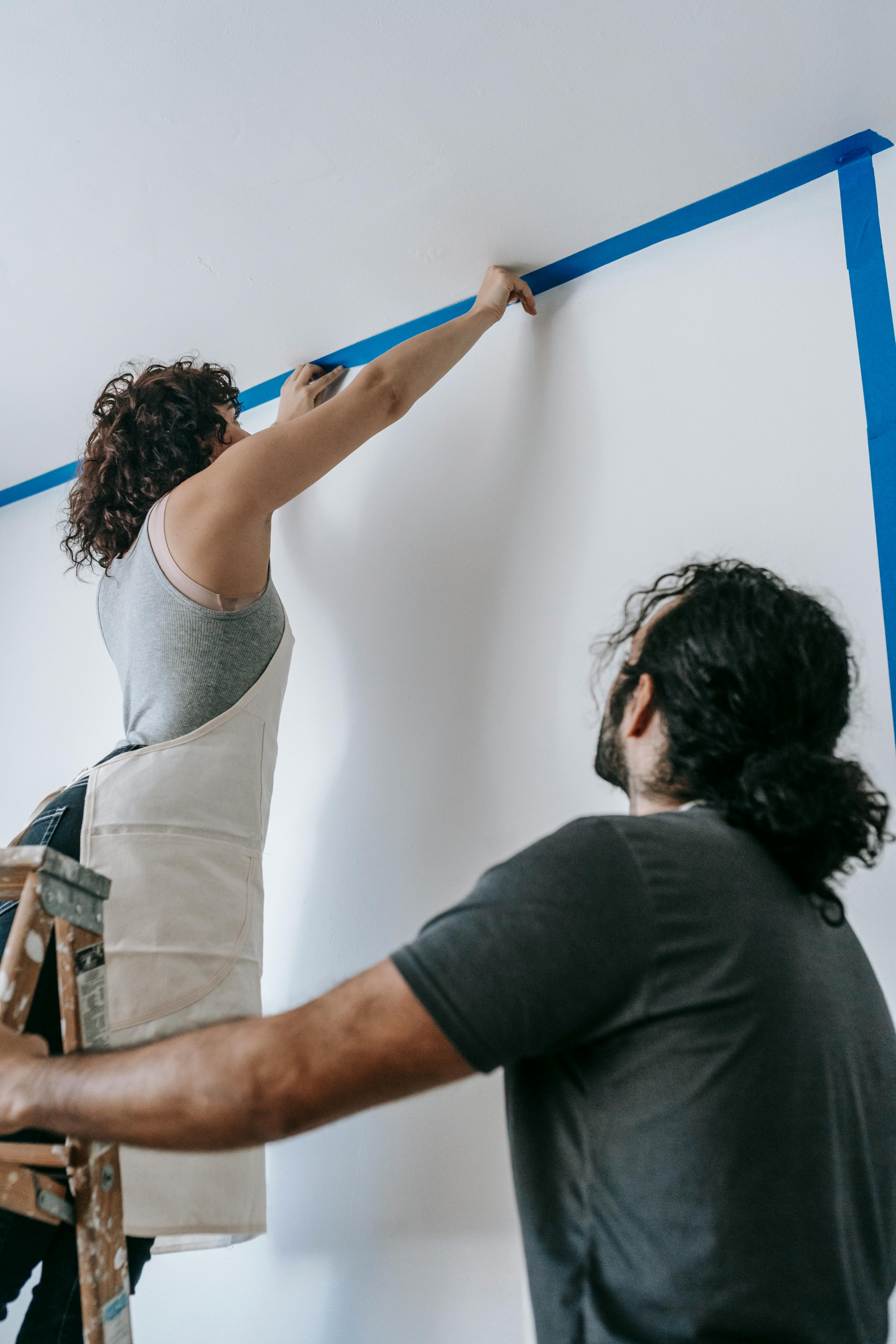 woman putting tape on wall and ceiling