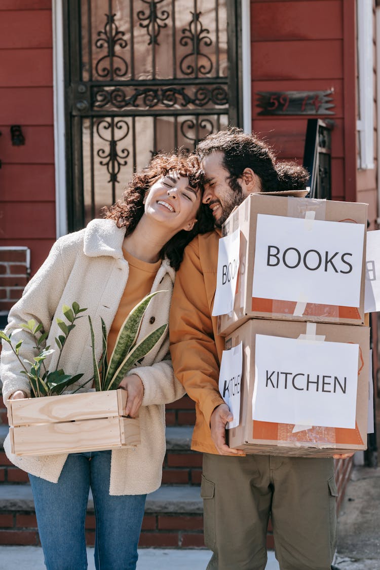 A Happy Couple Carrying Boxes And Plants