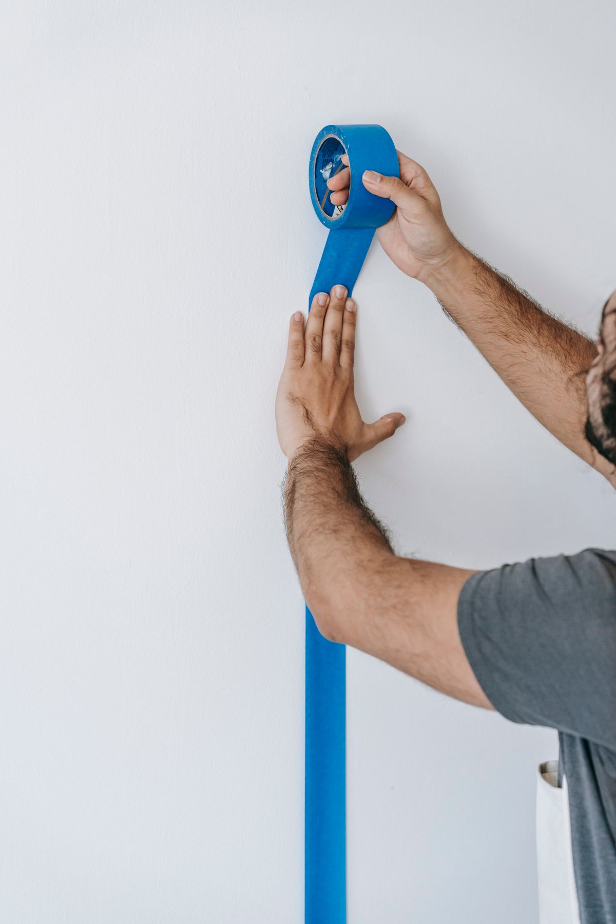 Hands pressing blue painter's tape along a wall edge