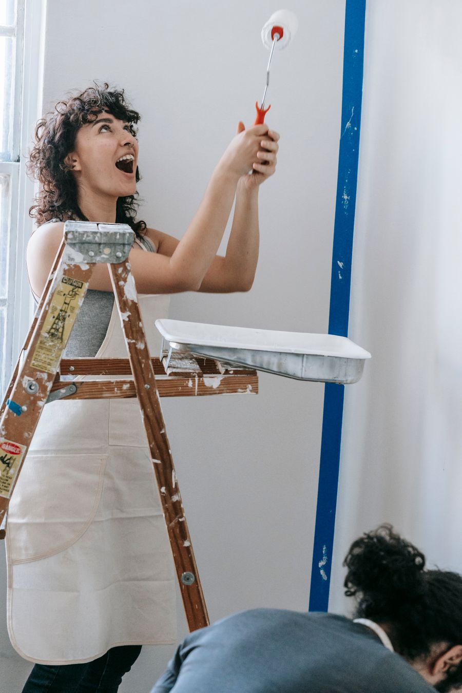 Painter rolling a fresh coat on an interior wall beside a ladder
