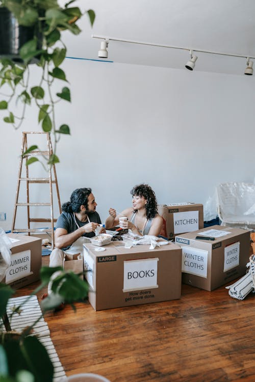 Couple Eating On Packed Boxes In A Room