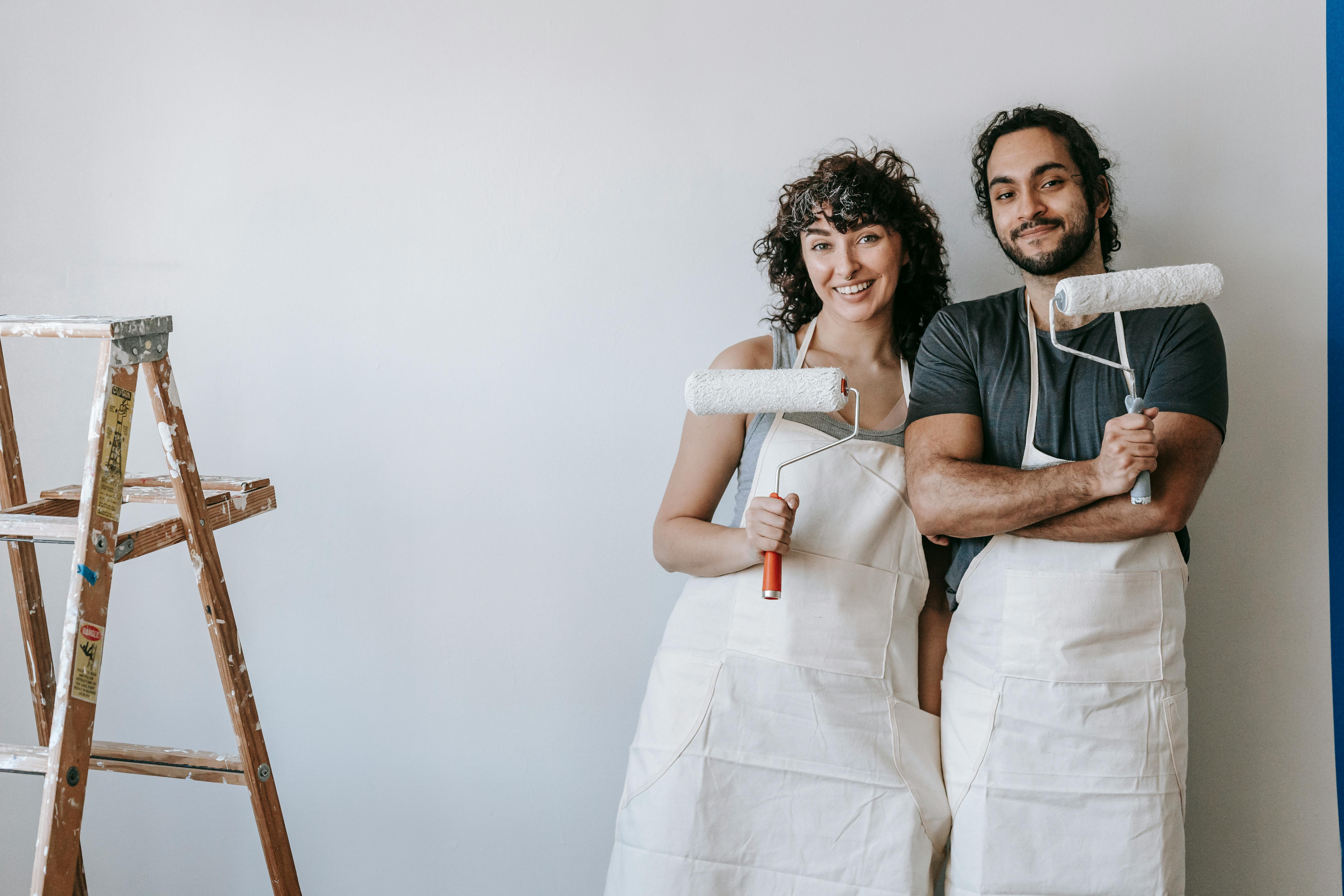 couple standing against the wall holding paint rollers