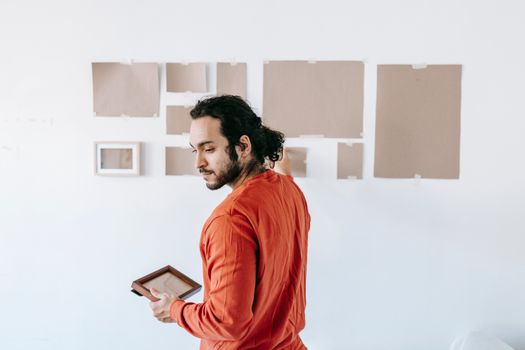 Man in a modern space holding a picture frame, suggesting relocation or renovation.