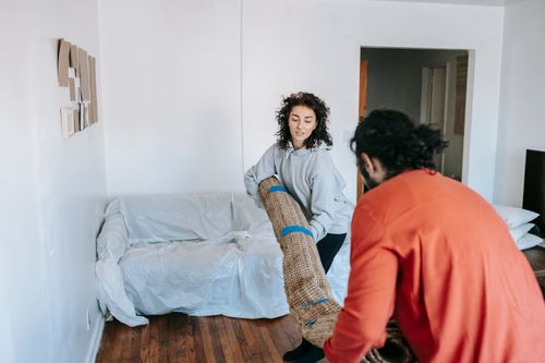Free A couple lifting a rolled carpet in a minimally furnished apartment living room. Stock Photo