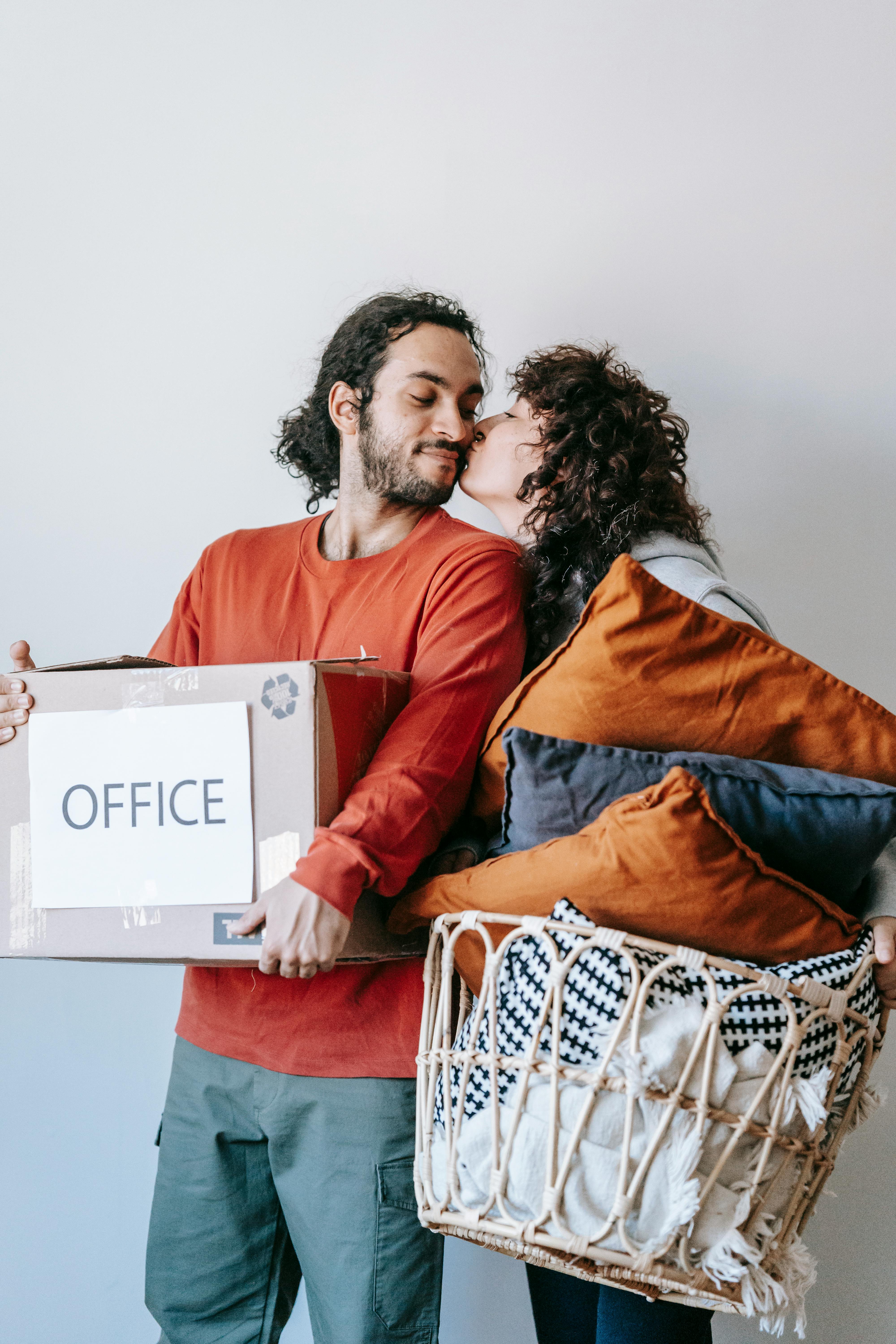 Woman Kissing A Man Carrying A Box Of Packed Office Supplies · Free Stock  Photo