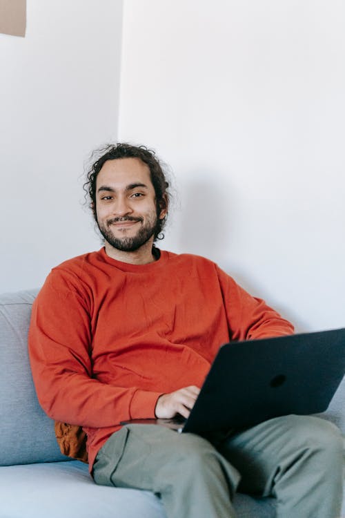 Free Man in Red Sweater Sitting on Couch With A Laptop Stock Photo