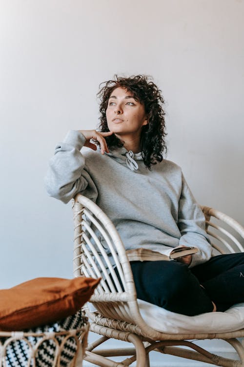 Woman in Gray Sweater Sitting on White Wicker Armchair