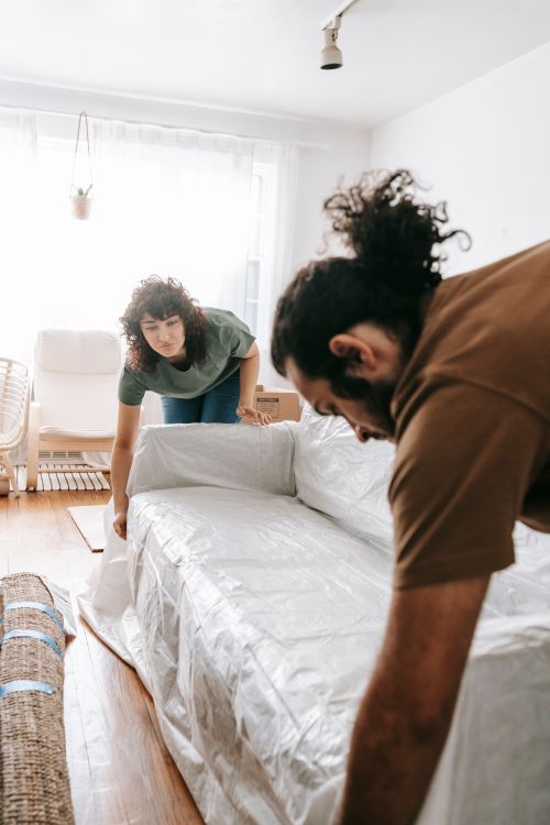 Free Two adults covering a couch during a home makeover or move. Stock Photo