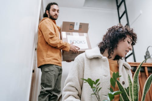 Man Carrying A Box And Woman With Plants