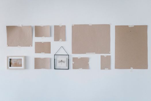 Collection of Kraft paper sheets and frames taped to a white wall in minimalist style.