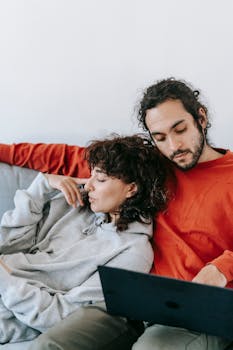 A cozy moment with a couple lounging on a couch using a laptop indoors.