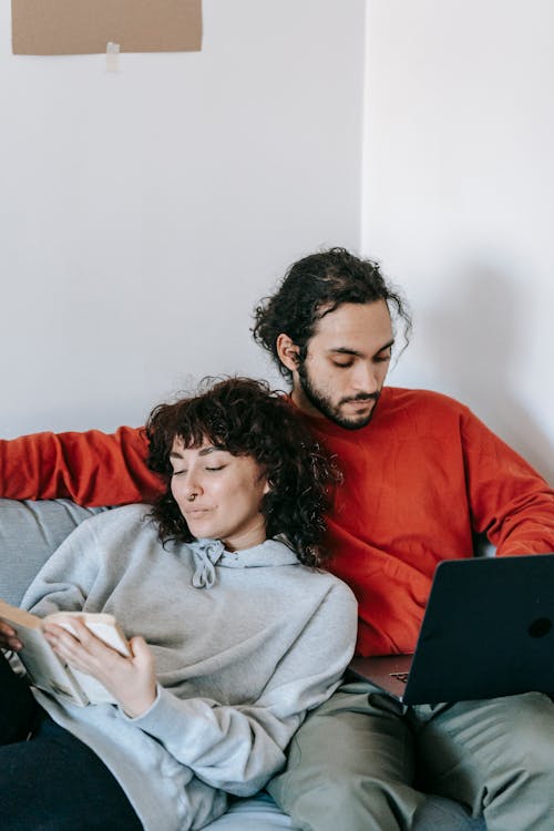 Free Ethnic couple with laptop and book resting on sofa Stock Photo