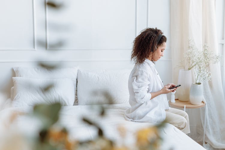 Woman Sitting On Bedside Using Cellphone With Headphone