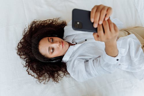 Woman Lying on Bed While Holding a Cellphone