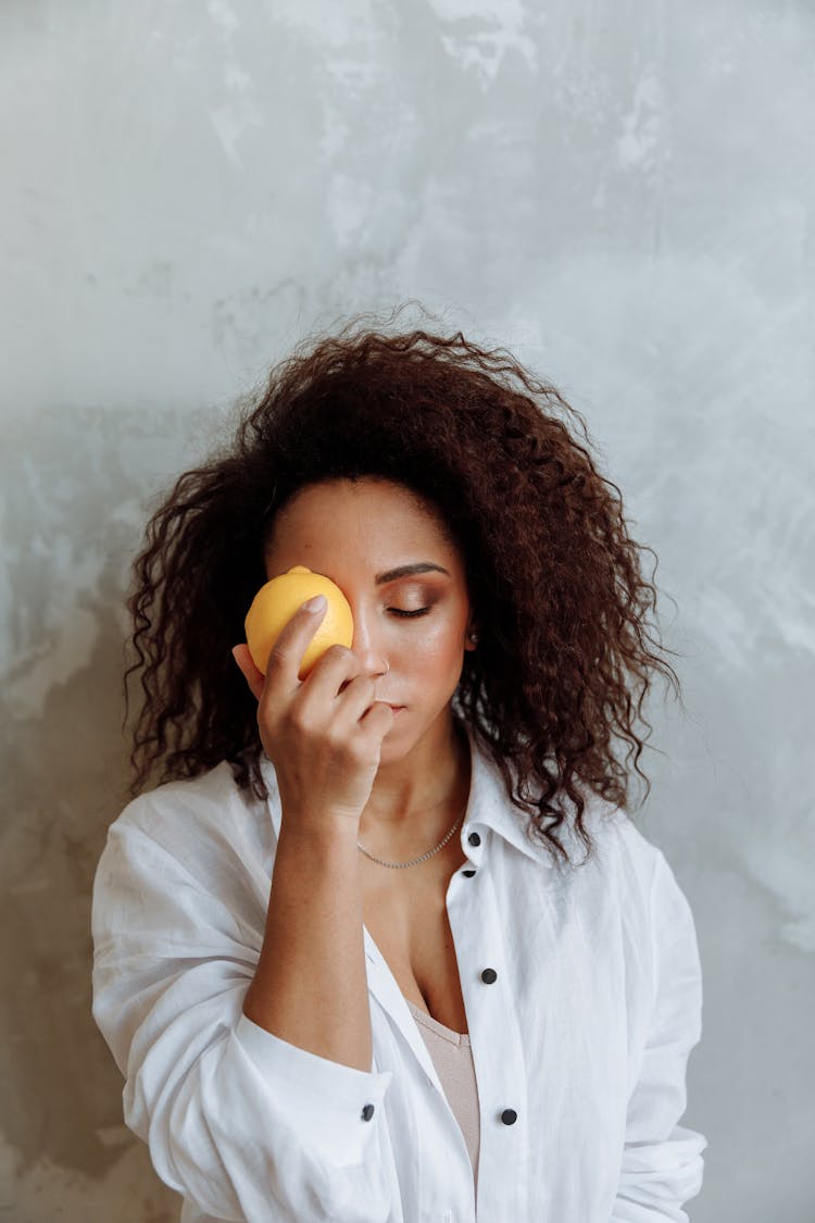 A Woman Placing A Lemon Fruit Over Her Eye