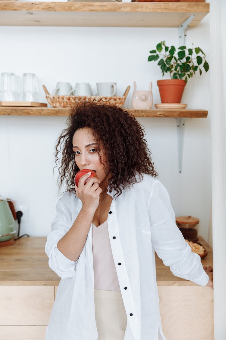 Woman In White Long Sleeves Biting An Apple 