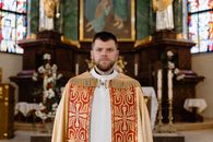 A priest in a decorated robe stands solemnly in a beautifully adorned church.