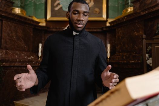 Priest in black vestment conducting a ceremony at a church altar with open book.