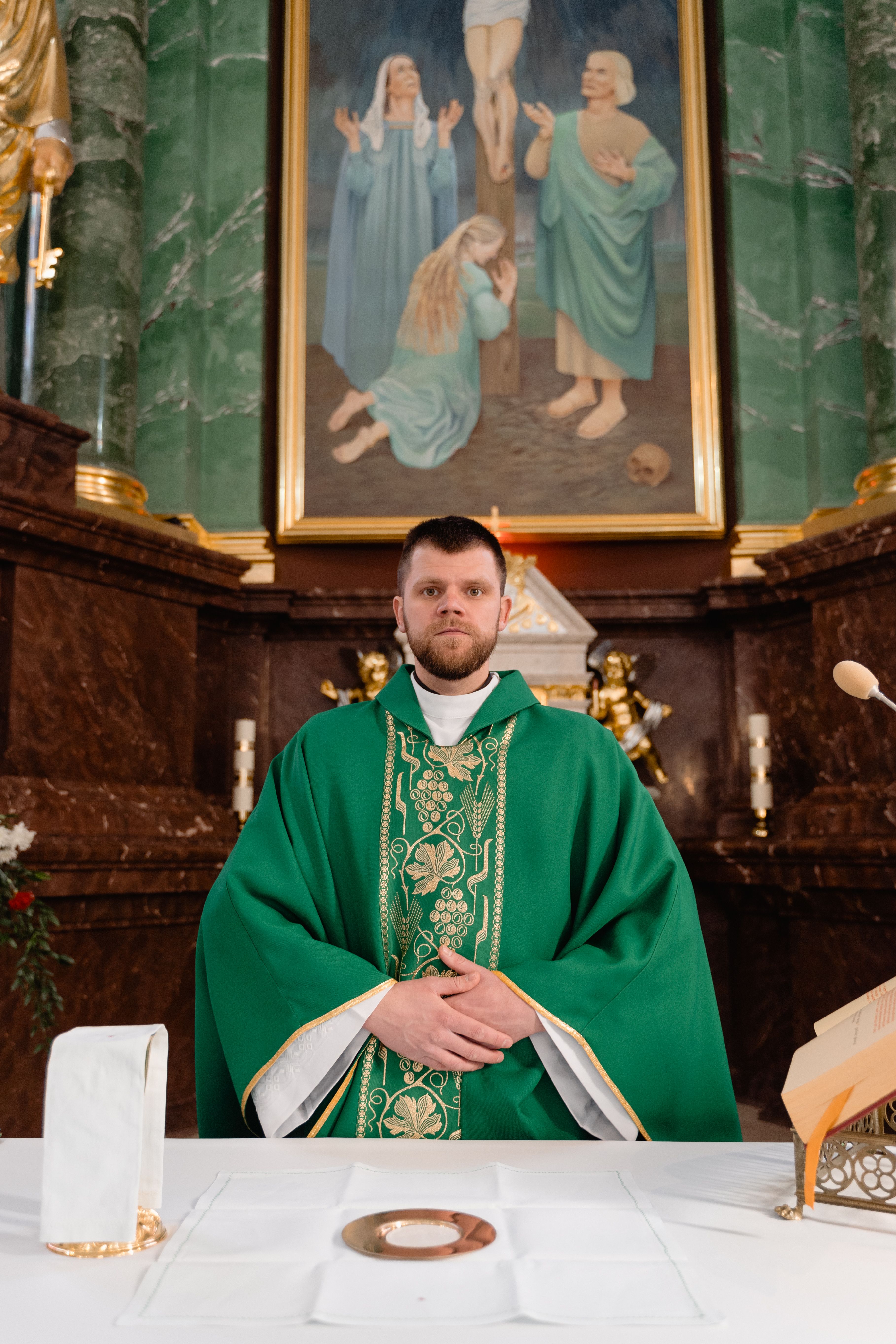 A Catholic priest stands at the altar in green chasuble with hands together in a church.