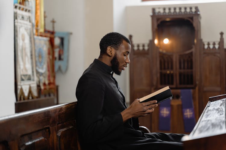 A Priest In Black Vestment Reading A Bible