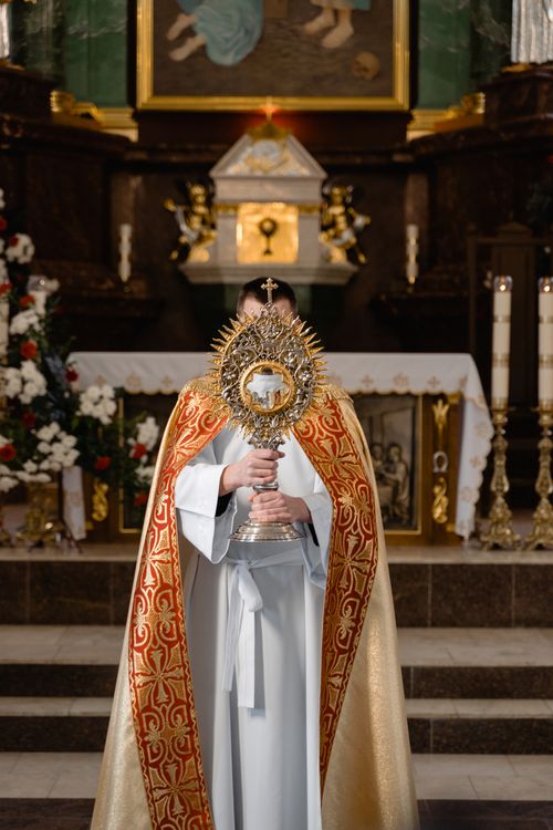 Free A priest in vestments holds a monstrance in front of a church altar, emphasizing solemn devotion. Stock Photo
