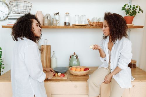 Free Two stylish women chatting and preparing fruit in a bright, modern kitchen. Stock Photo