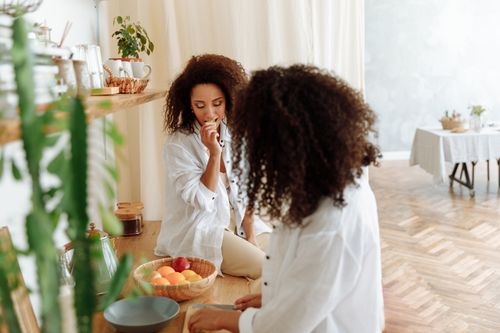 Free Two women enjoying a casual, stylish moment in a cozy kitchen setting with fresh fruits. Stock Photo
