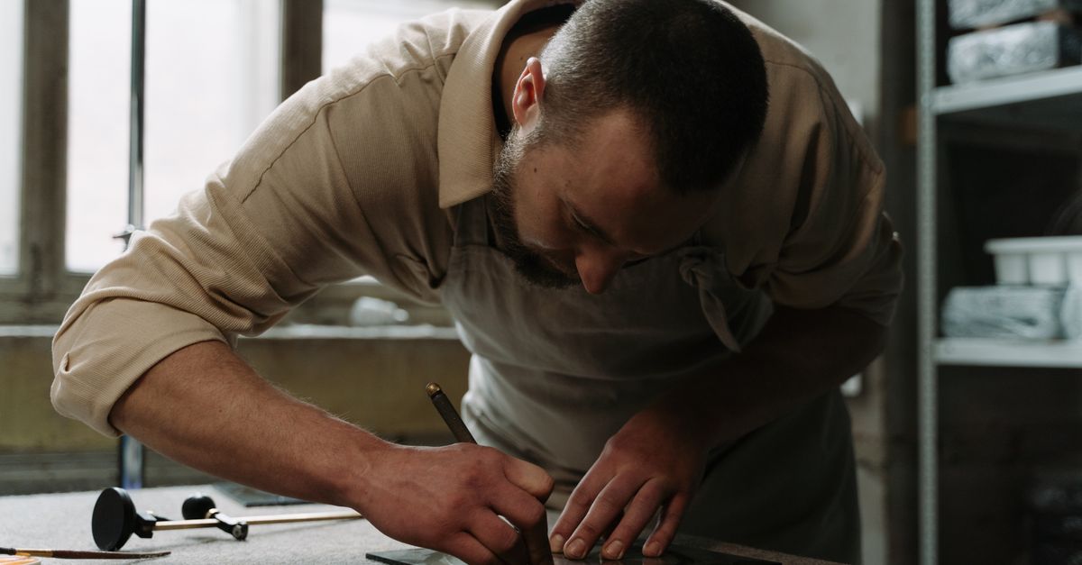 Craftsman measuring and cutting glass in a workshop — precision and accreditation underpin the consultative, trust-led sale of planned glazing work