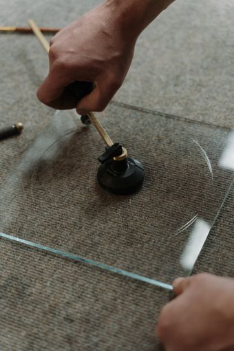 Close-up of an artisan scoring a sheet of glass with a hand cutter — photo by cottonbro studio on Pexels