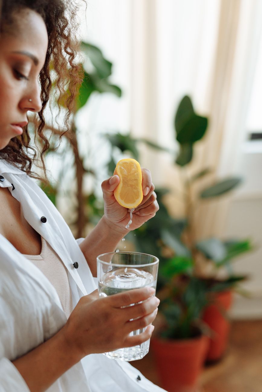 A woman squeezing lemon into a glass of water on a kitchen bench
