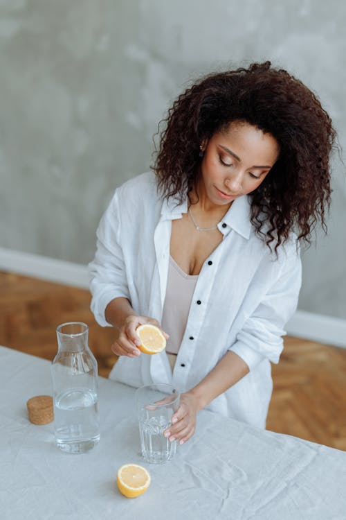 Free Woman with Curly Hair Holding a Glass of Water and a Slice of Lemon Stock Photo
