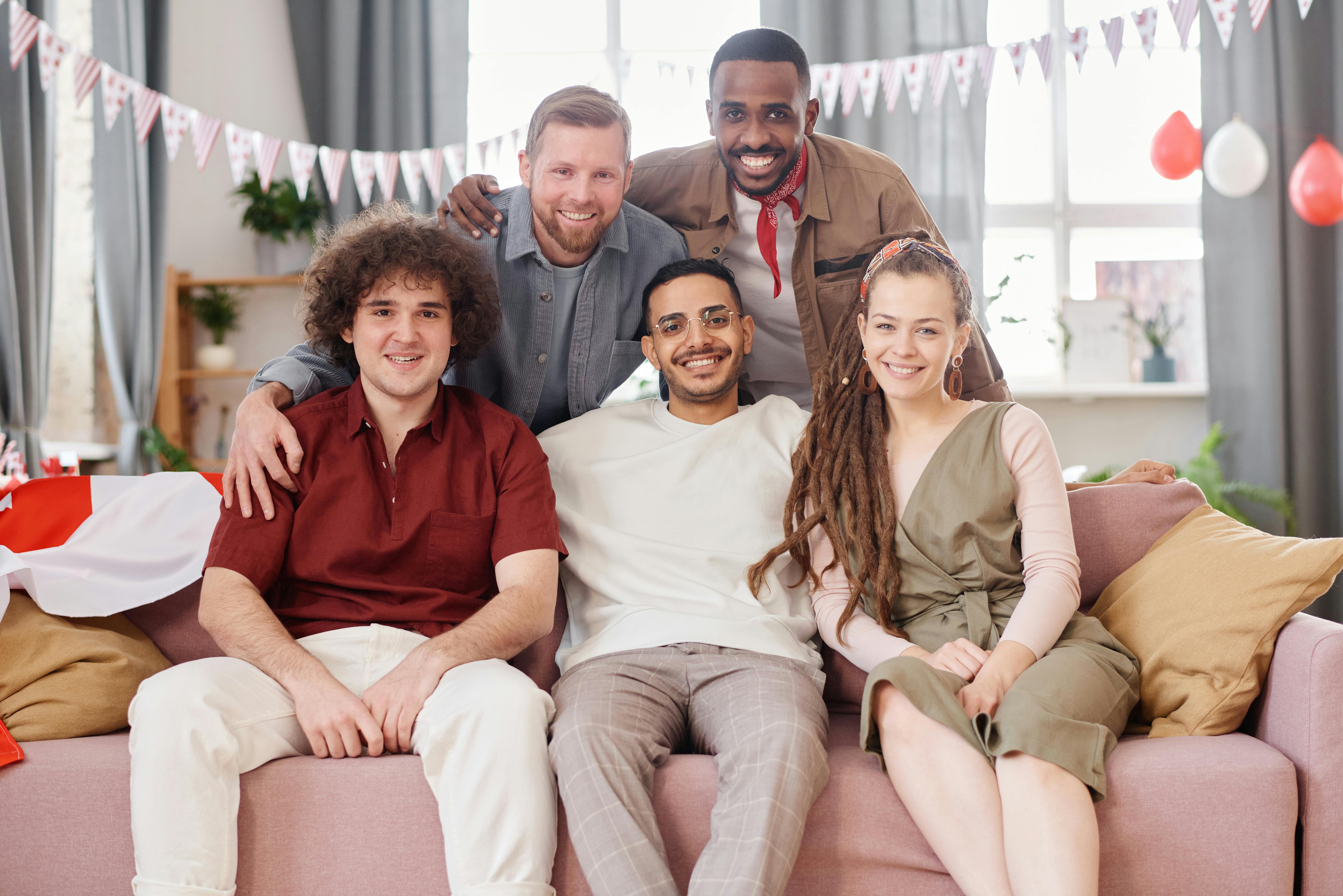 A cheerful and diverse group of young adults sitting together indoors, celebrating friendship.